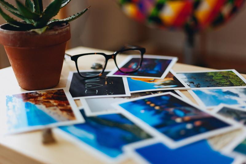 An image of a pair of glasses sitting on a table full of photos